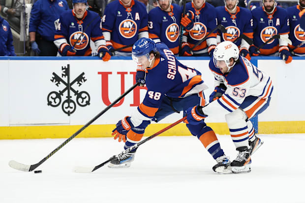 Hockey player in blue uniform shields puck from defender in whit
