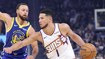 Phoenix Suns guard Devin Booker handles the ball while being defended by Golden State Warriors guard Stephen Curry.