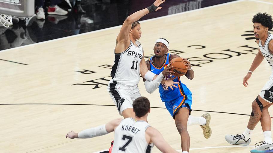 Oklahoma City Thunder guard Shai Gilgeous-Alexander drives while defended by San Antonio Spurs forward Carter Bryant.