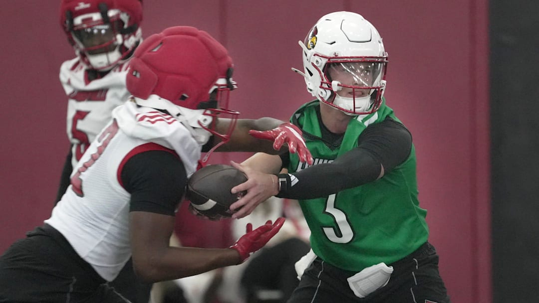 Louisville’s Lincoln Kienholz hands the ball off to Lekhy Thompkins in football practice at the Trager Center.