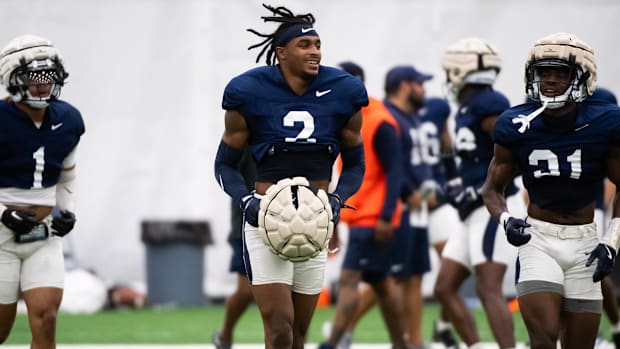 A Penn State football player runs across the practice field holding his helmet.