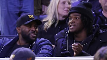 Dec 7, 2024; Ann Arbor, Michigan, USA;  Michigan Wolverines head coach football Sherrone Moore and quarterback commit Bryce Underwood talk in the first half of a basketball game against the Iowa Hawkeyes at Crisler Center. Mandatory Credit: Rick Osentoski-Imagn Images