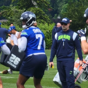 Seahawks offensive coordinator Ryan Grubb watches as quarterbacks Geno Smith and Sam Howell prepare to throw during a team drill at OTAs.