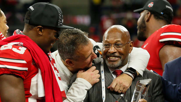 Head coach hugs former team legend who holds the trophy.