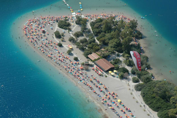 A beautiful scene showing a blue lagoon surrounding an island with many people on the beach.