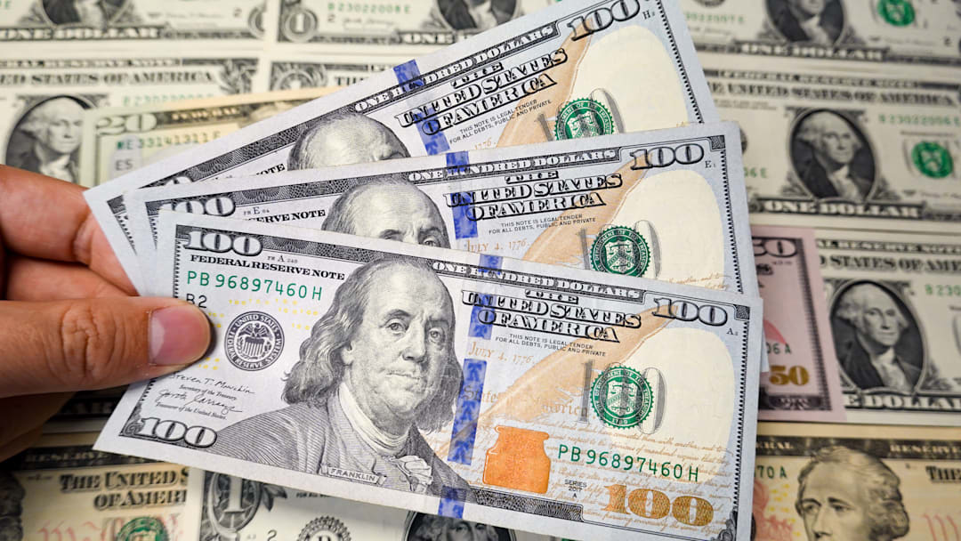 A hand holds several new $100 USD A hand holds several new $100 USD