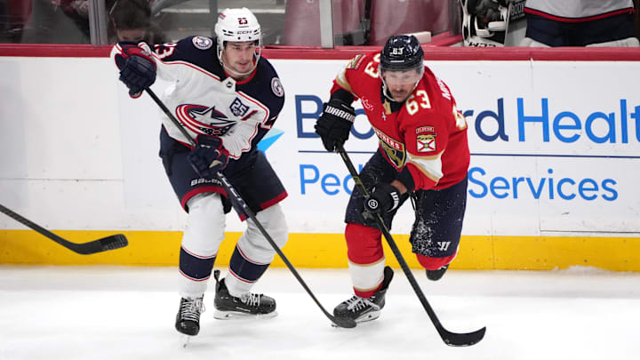 Blue Jackets center Sean Monahan chases after the puck alongside Panthers forward Brad Marchand.