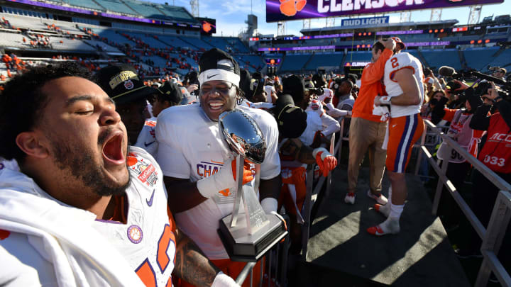 Clemson Tigers offensive lineman Bryn Tucker (73) and offensive lineman Zack Owens (72) celebrate with the Gator Bowl trophy while Clemson Head Coach Dabo Swinney hugs Clemson Tigers quarterback Cade Klubnik (2) after the team's close victory over Kentucky.