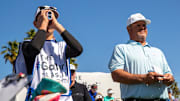 Ty Smock, 15, checks the range finder of his dad, Brian Smock, while caddying for him during the first round of The Galleri Classic at Mission Hills Country Club in Rancho Mirage, Calif., Friday, March 29, 2024.