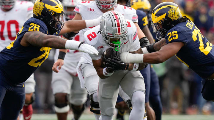 Nov 25, 2023; Ann Arbor, Michigan, USA; Michigan Wolverines defensive lineman Rayshaun Benny (26) and linebacker Junior Colson (25) tackle Ohio State Buckeyes wide receiver Emeka Egbuka (2) during the first half of the NCAA football game at Michigan Stadium. Mandatory Credit: Adam Cairns-USA TODAY Sports