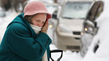 A woman wipes her brow while shoveling snow away from her car