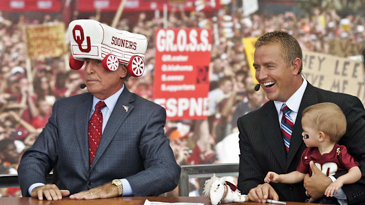 Sep 17, 2011; Tallahassee, FL, USA;  ESPN's College GameDay football analyst Lee Corso (left) dons an Oklahoma Sooners hat as his colleague Kirk Herbstreit (right) holds one of Corso's grandkids prior to the start of the Florida State Seminoles college football game against the Oklahoma Sooners at Doak Campbell Stadium. Corso had just predicted the Sooners would defeat the Seminoles. Mandatory Credit: Phil Sears-Imagn Images