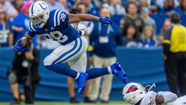 Colts running back Jonathan Taylor (blue and white uniform) runs over a defender attempting to tackle him.