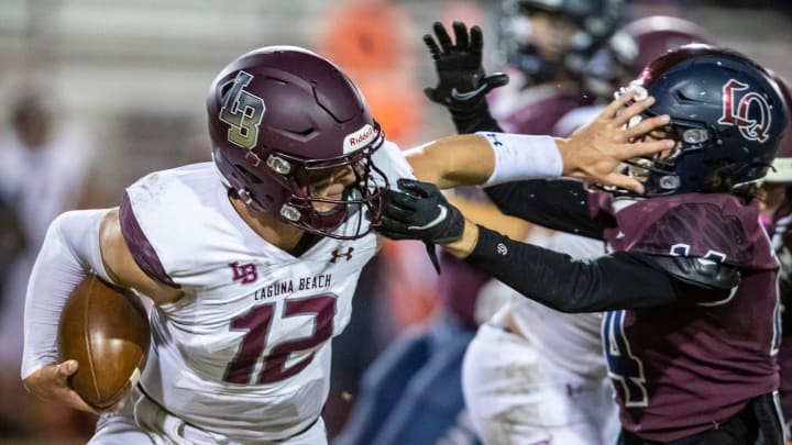 Laguna Beach's Jackson Kollock (12) stiff arms La Quinta's Calvin Miller (14) as he scrambles during the fourth quarter of their CIF-SS quarterfinal game in La Quinta, Calif., Friday, Nov. 11, 2022.