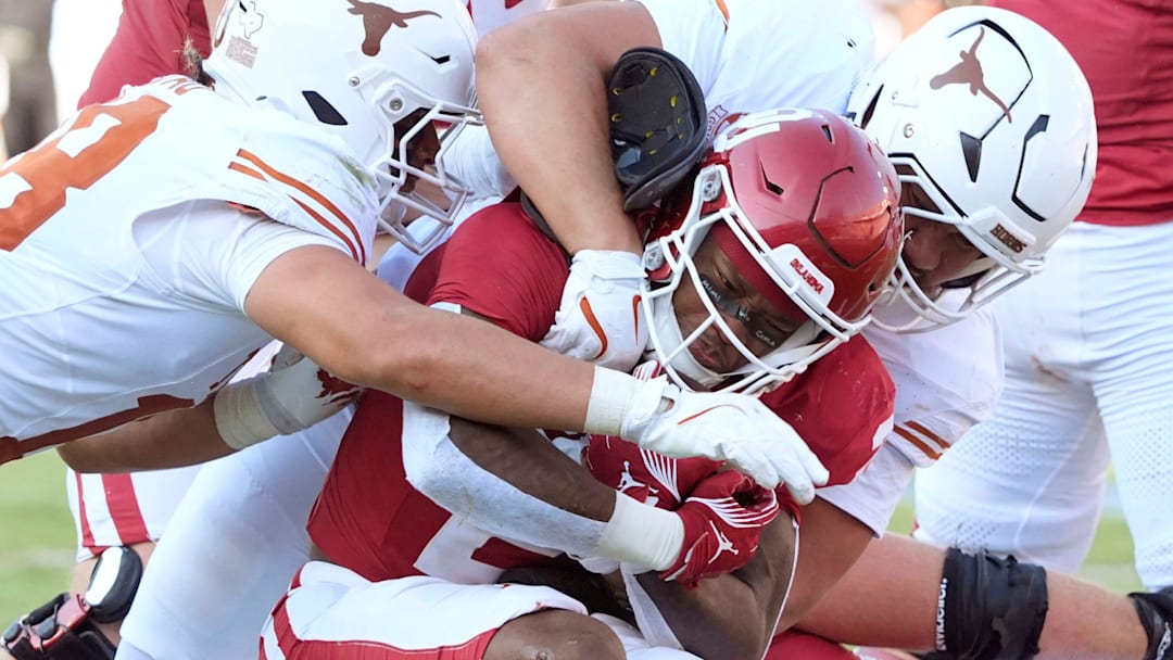 Oklahoma Sooners running back Jovantae Barnes (2) is brought down by Texas Longhorns linebacker Colin Simmons, bottom, linebacker Liona Lefau (18), left, and defensive lineman Jermayne Lole (99) during the Red River Rivalry college football game between the University of Oklahoma Sooners (OU) and the Texas Longhorns at the Cotton Bowl in Dallas, Saturday, Oct. 12, 2024. Texas one 34-3.