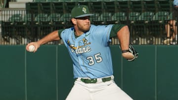 Pitcher winds up to throw baseball wearing green hat, blue jersey with number 35 and Tulane logo and white pants.
