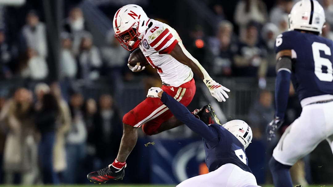 Nov 22, 2025; University Park, Pennsylvania, USA; Nebraska Cornhuskers running back Emmett Johnson (21) jumps to avoid a tackle from Penn State Nittany Lions cornerback A.J. Harris (4) during the first quarter at Beaver Stadium. Mandatory Credit: Matthew O'Haren-Imagn Images