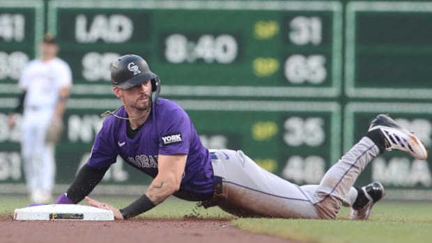 A baseball player in a purple and white uniform with a dark helmet sliding onto a white base on the field.