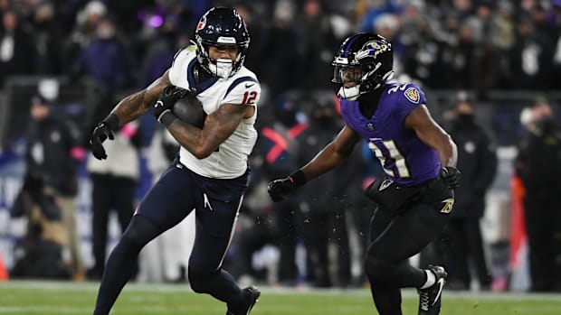 Texans receiver Nico Collins (white jersey; blue pants) runs away from a defender while carrying the football. 