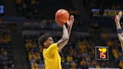 Feb 19, 2025; Morgantown, West Virginia, USA; West Virginia Mountaineers guard Jonathan Powell (11) shoots a three point shot over Cincinnati Bearcats forward Dillon Mitchell (23) during the second half at WVU Coliseum. Mandatory Credit: Ben Queen-Imagn Images