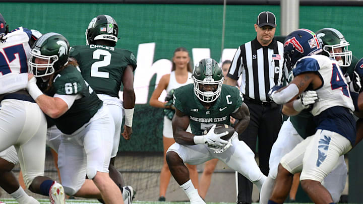 Aug 30, 2024; East Lansing, Michigan, USA;  Michigan State Spartans running back Nate Carter (5) drives through a hole in the line in the first quarter against the Florida Atlantic Owls at Spartan Stadium. Mandatory Credit: Dale Young-Imagn Images