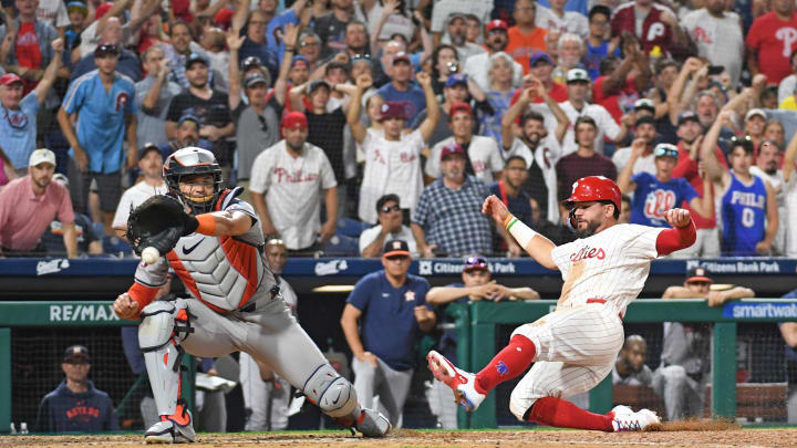 Aug 26, 2024; Philadelphia, Pennsylvania, USA; Philadelphia Phillies designated hitter Kyle Schwarber (12) slides safely into home as Houston Astros catcher Yainer Diaz (21) reaches for the throw during the tenth inning at Citizens Bank Park.