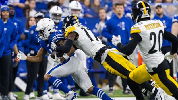 A Colts receiver runs away from Steelers defenders (white jerseys/black helmets) wearing a blue jersey and white helmet.