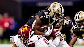 Dec 15, 2024; New Orleans, Louisiana, USA;  New Orleans Saints running back Kendre Miller (25)  is tackled by Washington Commanders cornerback Mike Sainristil (0) during the second half at Caesars Superdome. Mandatory Credit: Stephen Lew-Imagn Images