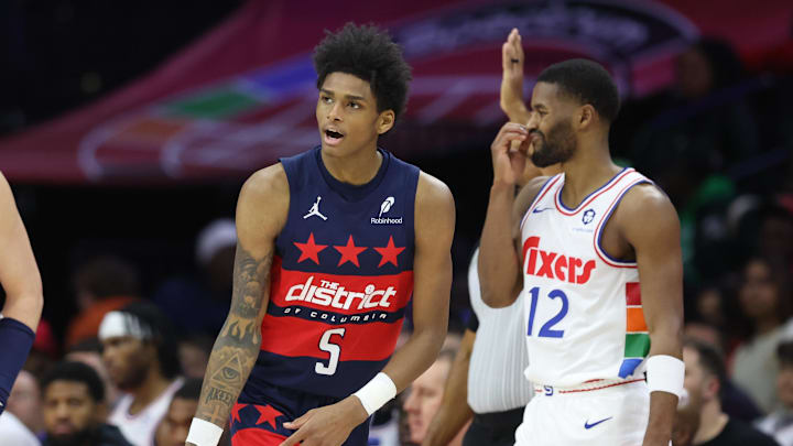 Mar 26, 2025; Philadelphia, Pennsylvania, USA; Washington Wizards guard AJ Johnson (5) reacts to his three pointer in front of Philadelphia 76ers guard Jared Butler (12) during the fourth quarter at Wells Fargo Center. Mandatory Credit: Bill Streicher-Imagn Images