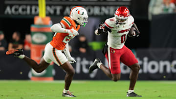 Oct 17, 2025; Miami Gardens, Florida, USA; Louisville Cardinals wide receiver Chris Bell (0) carries the football against Miami Hurricanes defensive back Jr. Romanas Frederique (29) during the second quarter at Hard Rock Stadium. Mandatory Credit: Sam Navarro-Imagn Images
