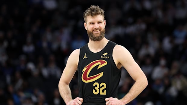 A basketball smiling with his hands on his hips while wearing a black uniform.