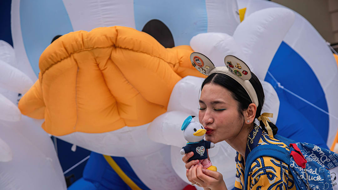 A woman kisses a Donald Duck doll and poses for a photo in...