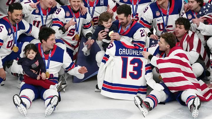 Feb 22, 2026; Milan, Italy; Zach Werenski (bottom left) of the United States celebrates while holding Noa Gaudreau, the daughter of the late Johnny Gaudreau while Dylan Larkin (21) holds Johnny Gaudreau Jr after winning the men's ice hockey gold medal game during the Milano Cortina 2026 Olympic Winter Games at Milano Santagiulia Ice Hockey Arena. Mandatory Credit: James Lang-Imagn Images