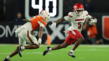Oct 17, 2025; Miami Gardens, Florida, USA; Louisville Cardinals wide receiver Caullin Lacy (5) carries the football against Miami Hurricanes safety Zechariah Poyser (7) during the first quarter at Hard Rock Stadium. Mandatory Credit: Sam Navarro-Imagn Images