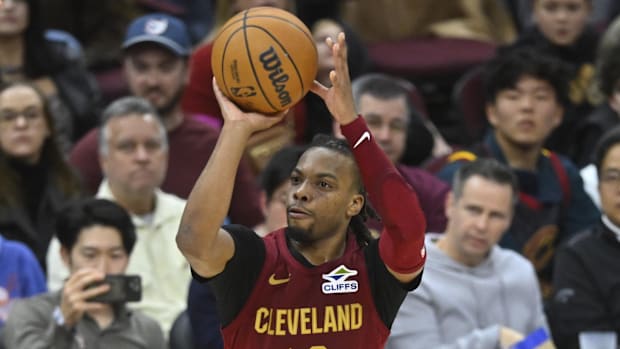 A basketball player shooting a basketball while wearing a wine and gold uniform.