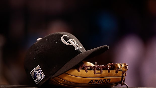 A black and purple Colorado Rockies hat sits on top of a tan glove.
