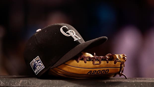 A black hat with the white Colorado Rockies logo on it sitting on a light brown baseball glove
