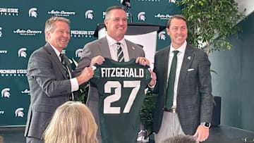 Michigan State Spartans head coach Pat Fitzgerald, center, poses with a namesake jersey next to MSU president Kevin Guskiewicz, left, and athletic director J Batt, right, during Fitzgerald's introductory press conference on Tuesday, Dec. 2, 2025.