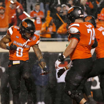 Nov 25, 2023; Stillwater, Oklahoma, USA;  Oklahoma State's Ollie Gordon II (0) celebrates with Oklahoma State's Preston Wilson (74) and Rashod Owens (10) after scoring a touchdown during the second overtime against the Brigham Young Cougars at Boone Pickens Stadium. Mandatory Credit: Sarah Phipps-USA TODAY Sports