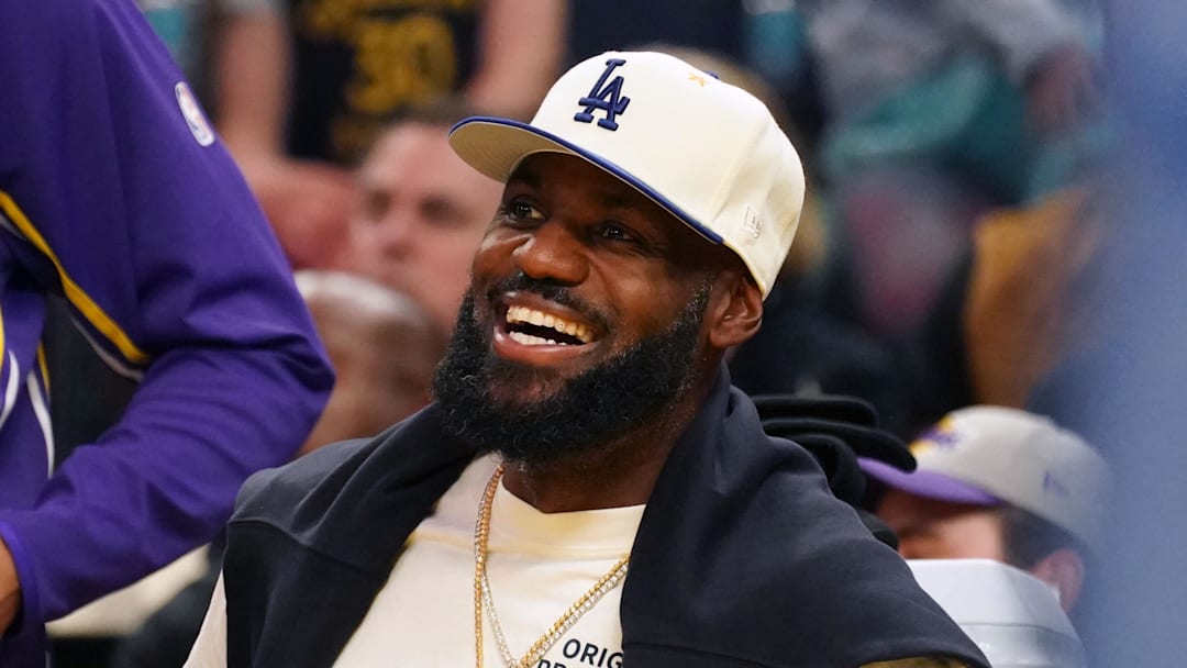 Oct 5, 2025; San Francisco, California, USA;  Los Angeles Lakers forward LeBron James (23), wearing a Los Angeles Dodgers hat, smiles after watching his son, guard Bronny James (9), dunk a rebound against the Golden State Warriors in the third quarter at Chase Center. Mandatory Credit: David Gonzales-Imagn Images