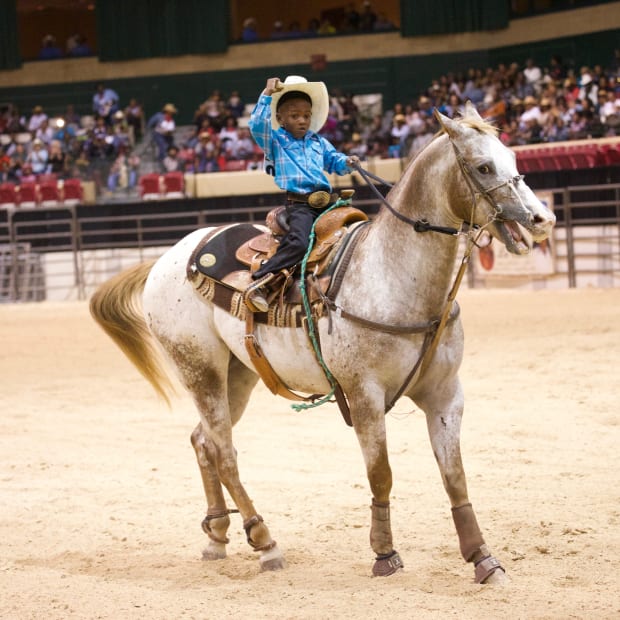 A little boy riding a roan horse.