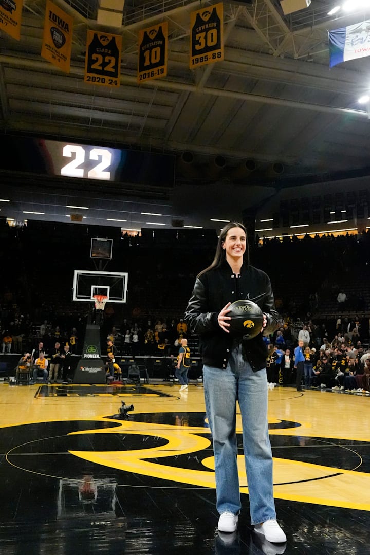 Caitlin Clark is pictured at half court as her retired jersey hangs in the rafters behind her at Carver-Hawkeye Arena.
