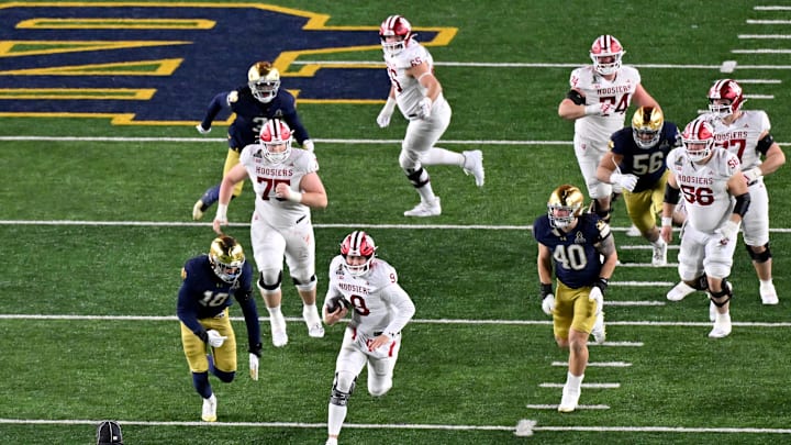 Dec 20, 2024; Notre Dame, Indiana, USA; Indiana Hoosiers quarterback Kurtis Rourke (9) runs past Notre Dame Fighting Irish defensive lineman Loghan Thomas (10) and defensive lineman Joshua Burnham (40) during the second half at Notre Dame Stadium. Mandatory Credit: Matt Cashore-Imagn Images