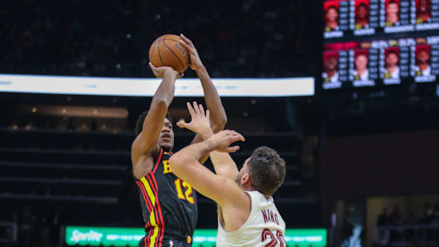 A basketball player wearing a black uniform shooting a basketball over another basketball player wearing a white uniform.