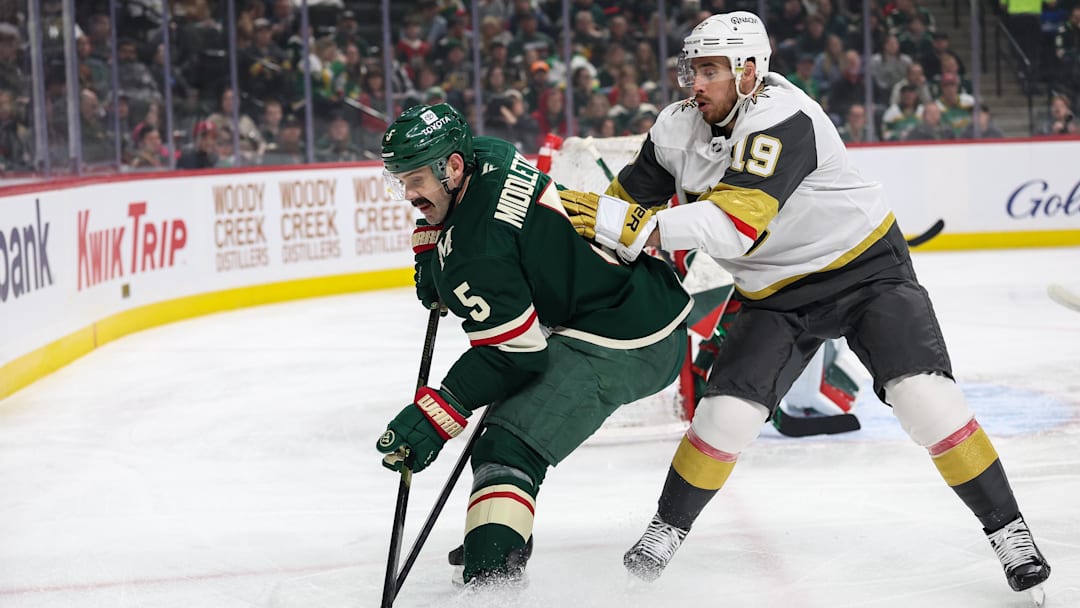 Mar 25, 2025; Saint Paul, Minnesota, USA; Minnesota Wild defenseman Jake Middleton (5) and Vegas Golden Knights right wing Reilly Smith (19) compete for the puck during the first period at Xcel Energy Center. Mandatory Credit: Matt Krohn-Imagn Images