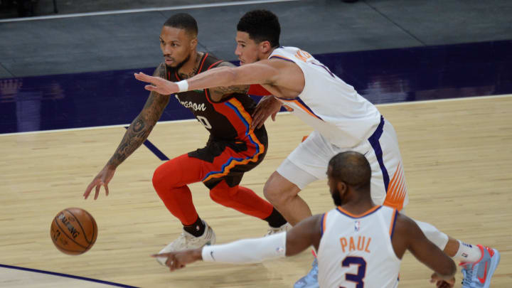 Feb 22, 2021; Phoenix, Arizona, USA; Portland Trail Blazers guard Damian Lillard (0) dribbles against Phoenix Suns guard Devin Booker (1) during the first half at Phoenix Suns Arena. Mandatory Credit: Joe Camporeale-USA TODAY Sports