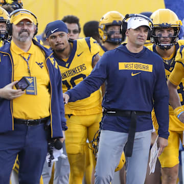 Sep 7, 2024; Morgantown, West Virginia, USA; West Virginia Mountaineers head coach Neal Brown talks with West Virginia Mountaineers quarterback Garrett Greene (6) after he threw for a touchdown during the second quarter against the Albany Great Danes at Mountaineer Field at Milan Puskar Stadium. Mandatory Credit: Ben Queen-Imagn Images