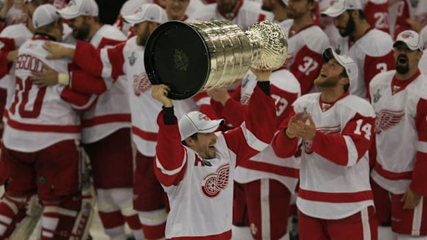 Hockey player in white uniform lifts Stanley Cu
