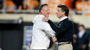 Oklahoma's Cale Gundy, co-offensive coordinator/inside receivers coach, and Oklahoma State coach Mike Gundy talk before a Bedlam college football game between the Oklahoma State University Cowboys (OSU) and the University of Oklahoma Sooners (OU) at Boone Pickens Stadium in Stillwater, Okla.,