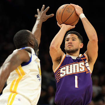 Apr 8, 2025; Phoenix, Arizona, USA; Phoenix Suns guard Devin Booker (1) shoots the ball over Golden State Warriors forward Draymond Green (23) during the second half at Footprint Center. Mandatory Credit: Mark J. Rebilas-Imagn Images
